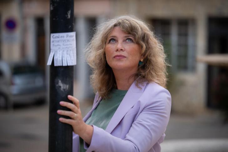 Cécile Bois se tenant à un lampadaire sur lequel apparaissent des étiquettes détachables à son nom